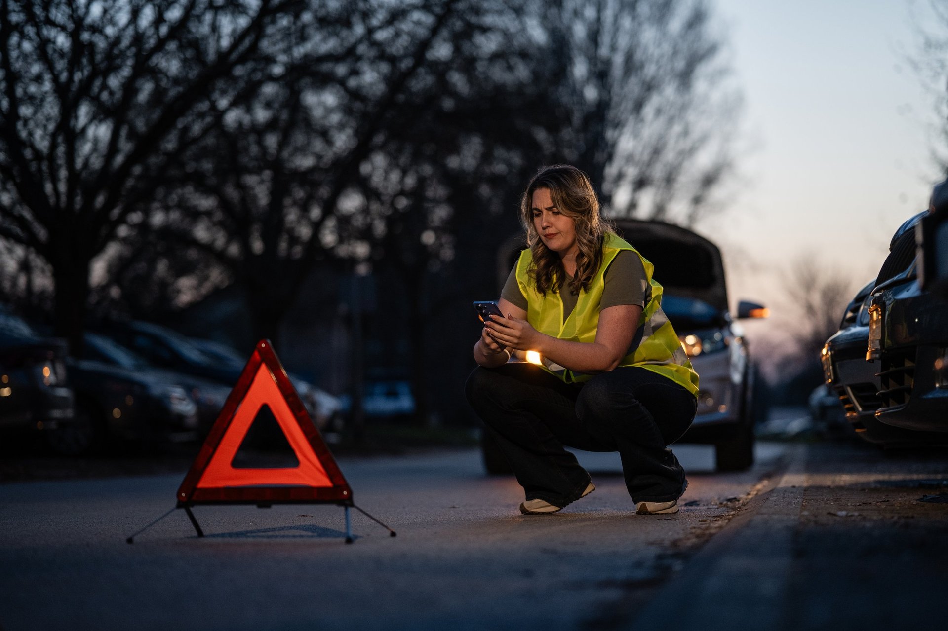Woman by broken car at dusk waiting for roadside help