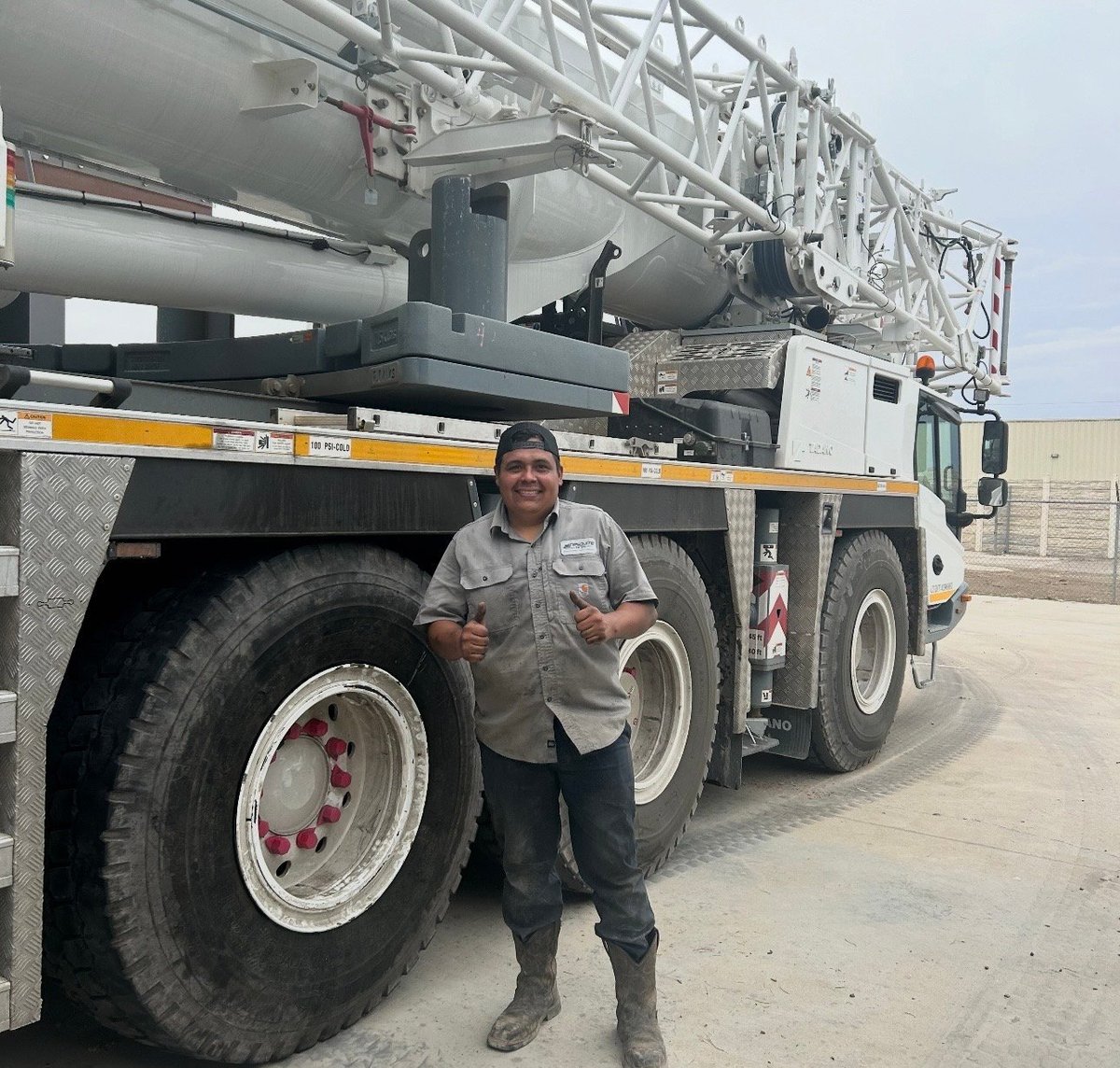 Worker posing in front of a large industrial concrete pump truck with extended boom arm