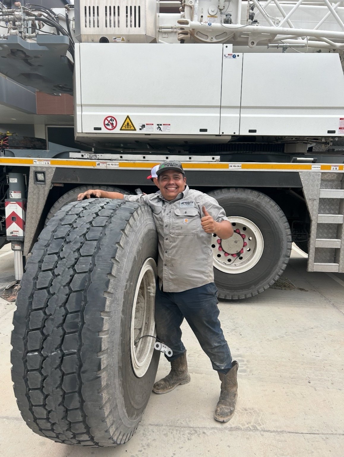 Truck driver posing next to a large heavy-duty tire in front of a commercial semi truck